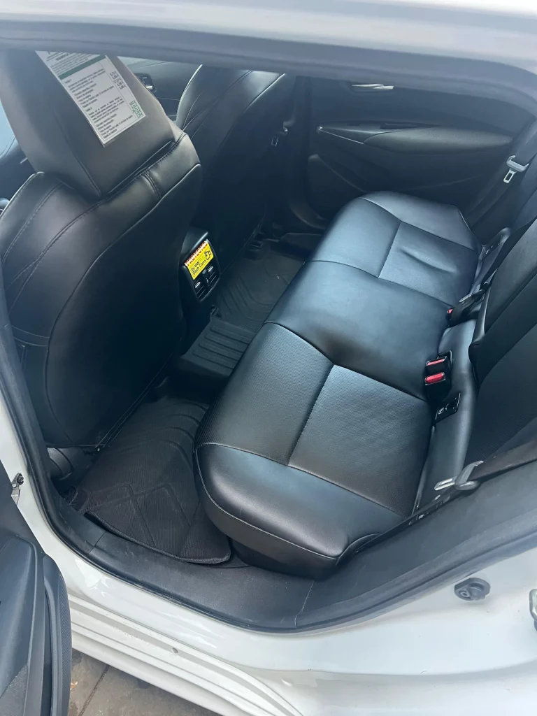 Interior de coche mostrando asientos traseros de cuero negro con puerta abierta