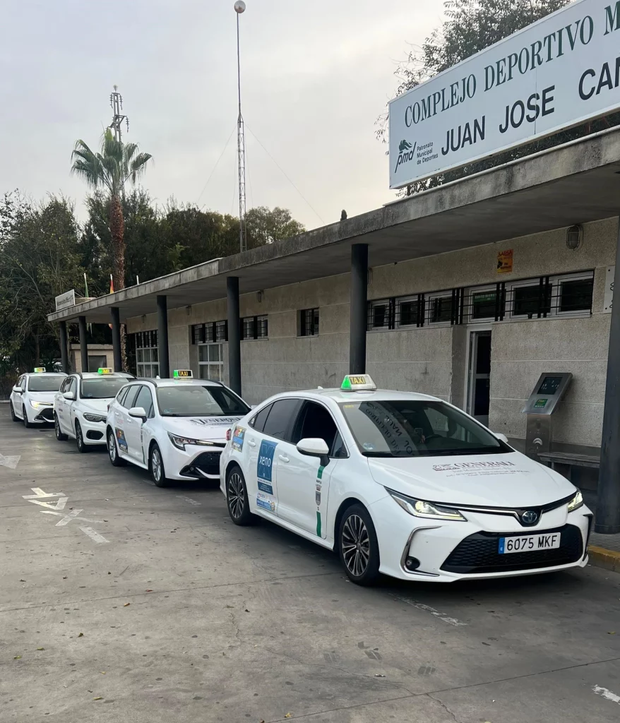 Cuatro taxis blancos alineados en el Complejo Deportivo Municipal Juan José Cano